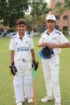 Two young cricket players in uniforms posing in a field in Sindh, Pakistan.